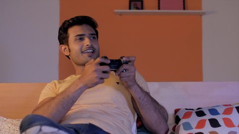 Portrait of smiling young man with stubble enjoying playing a video game. Closeup shot of excited Indian male playing a modern game with good graphics while relaxing in the bedroom