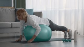 Older Lady Exercising Lying On Swiss Ball Spreading Hands Having Fitness Workout At Home. Active Sporty Senior Female Enjoying Training On Fitball Indoor. Slow Motion