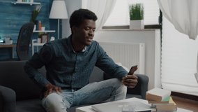 African american guy on online video call using phone in bright living room, internet online user working from home, connection with world for office communication and project planning