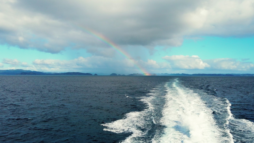 Traveling Through Blue Ocean In Bay Of Islands At New Zealand With Distant View Of Rainbow In Background. - Pullback Shot