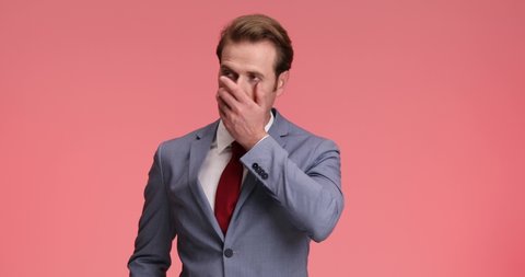 disappointed young businessman in elegant suit hearing bad news, touching forehead and worrying, nodding in a negative manner on pink background in studio