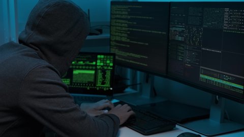 Unrecognizable man hacker wearing sweatshirt with hood typing on computer keyboard and breaking password. Side view of dangerous hooded computer hacker infecting system