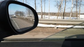 Video shooting in motion, view in the rear view side mirror of a auto, driving a red car along the road, on a snowy winter day