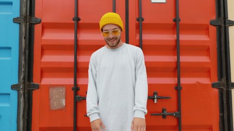 Happy Funny young man dancer moves beautifully to music smiling yellow beanie hat background of bright red containers summer. Charismatic people. Rhythmic dances of professional dancer. Positive Party