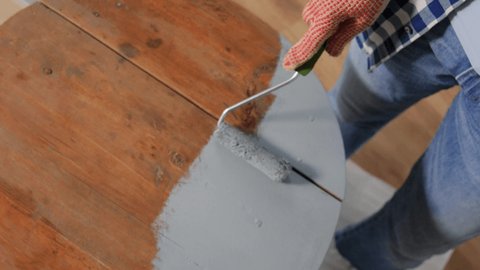 furniture renovation, diy and home improvement concept - woman in gloves with paint roller painting old wooden table to grey color