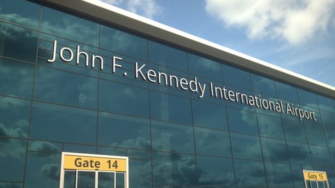Landing airplane reflects in the modern windows with John F. Kennedy International Airport text