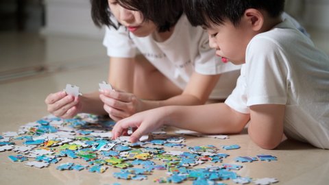 Asia family, Mother and son lying on the floor doing jigsaw puzzles game. Woman and boy finding the piece of jigsaw during work at home. Woman teaches child to solve puzzles. Cheerful concept