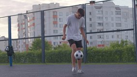 Young caucasian amateur man practicing soccer skills and tricks with the football ball at sunset in an playground. Urban city lifestyle outdoors concept. 4K UHD slow motion RAW graded footage