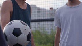 Close up of young happy smiling amateur football players perform tricks with the soccer ball before to start a friendly match or training workout game on court in a sunny day. 4K RAW graded footage