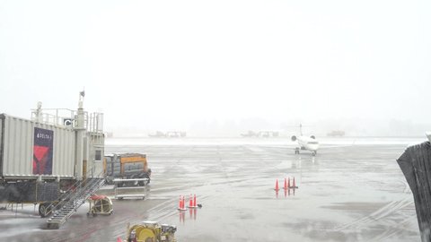 Minneapolis, MN - 03 15 2021: 4K clip showing line of airport snow removal equipment driving down snowy runway at Minneapolis airport. Parked Delta airplane in foreground. Foggy. 