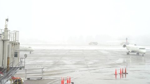 Minneapolis, MN - 03152021: 4K clip showing line of airport snow removal equipment driving in the distance down snowy runway at Minneapolis airport. Two Delta airplanes in foreground, one driving away