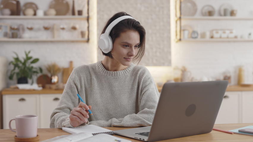 Pretty young woman wearing wireless headphones and using laptop for online studying at home. Video conversation for self education. Royalty-Free Stock Footage #1073790671