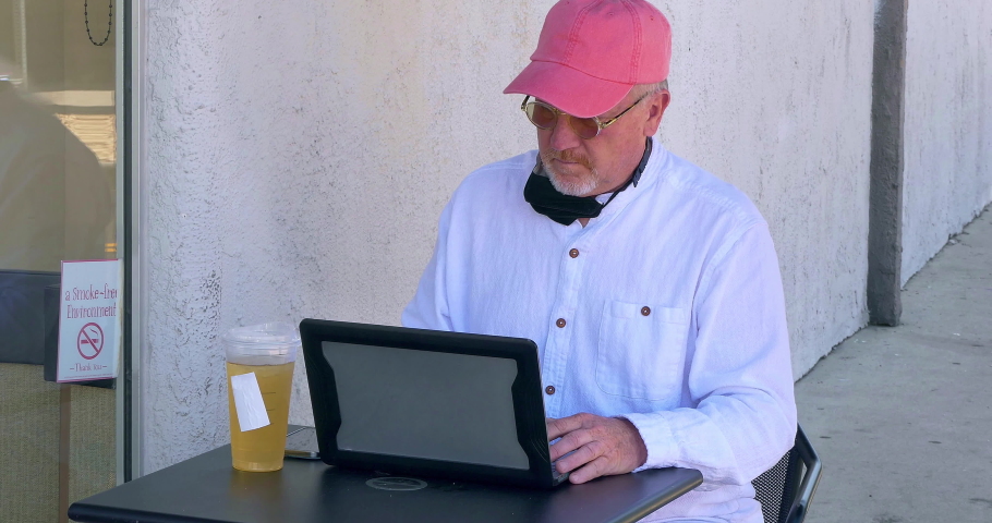 Mature senior man in casual dress browsing social media on a laptop computer at outside cafe in Los Angeles, California, 4K