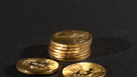 Close up one golden bitcoin physical coin spins and falls from coin stack over black background, slow motion