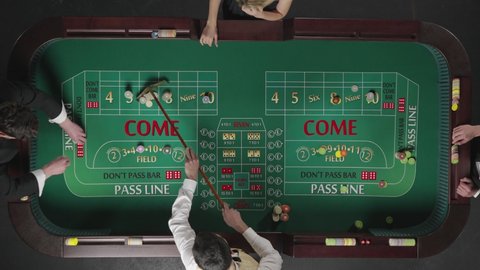 Top view of two men and a woman playing craps while sitting at a table in a casino. Players place bets with chips. The man throws the dice and wins. Slow motion ready, 4K at 59.94fps.
