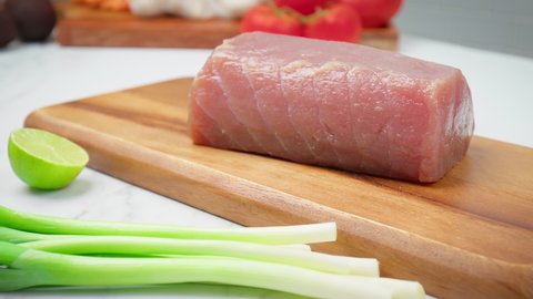 Closeup of raw Tuna Yellowfin on a table with greens and vegetables in 4K. Healthy meat, fresh tuna for steak or salad on a chopping board.