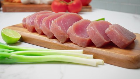 Closeup of Sliced Raw Tuna Yellowfin on a table with greens and vegetables in 4K. Healthy meat, fresh tuna cut in pieces on a chopping board.