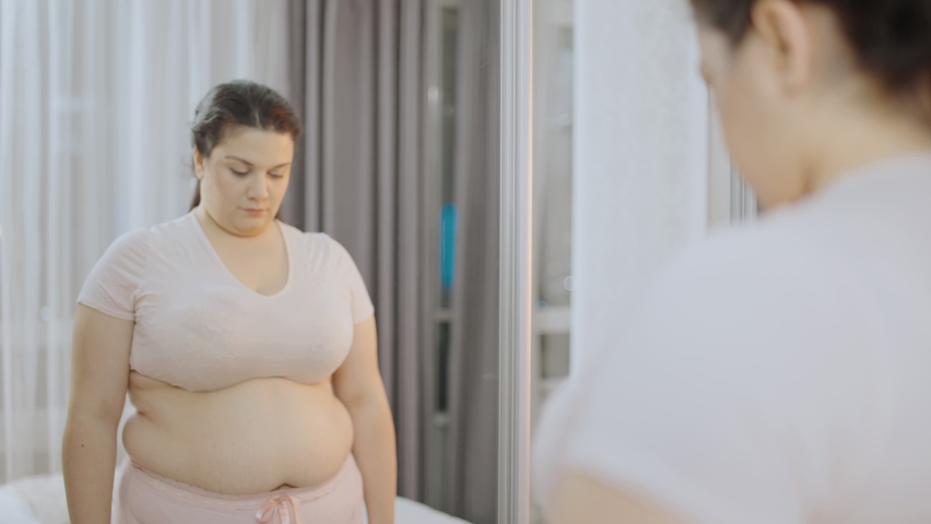 Desperate chubby woman with excess belly fat looking at mirror, insecurities | Shutterstock HD Video #1073797421
