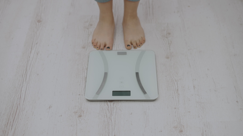 Sad plus size female standing on scales, feeling upset about weight gain, body