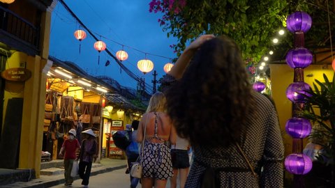 LOCAL PEOPLE AND TOURISTS AT NIGHT ON THE STREETS OF HOI AN, VIETNAM – 6 APRIL 2018: Local people, tourists and bicycle rickshaws at night on the streets of Hoi An, Vietnam