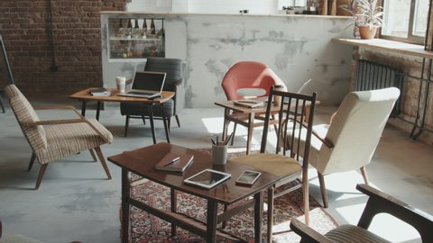 No people overview of gadgets, coffee cups, notebooks and other stationery on work desks in stylish loft coworking space with designer furniture and chairs under sunlight