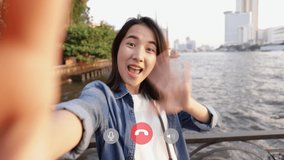 Attractive of Asian female taking selfie video chat with her friends sharing enjoyment vacation summer traveling in Bangkok Thailand while standing beside Chao Phraya River in Thailand.