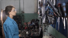 A woman car mechanic in work clothes stands near a stand with wrenches. Selects the required size. Automotive workshop concept. - Powered by Shutterstock - Get 15% off with code: PIKWIZARD15