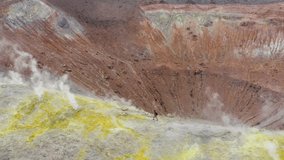 Scenic view of man walking trough volcano sulfuric smokes, tilt down camera toward crater. Volcano Island travel destination in Sicily, Aeolian Islands. Aerial pan