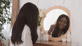 Haircare. Happy African American Woman Brushing Hair Sitting Near Mirror, Smiling To Her Reflection At Home. Female Combing Hair With Hairbrush. Beauty Care Concept. Selective Focus