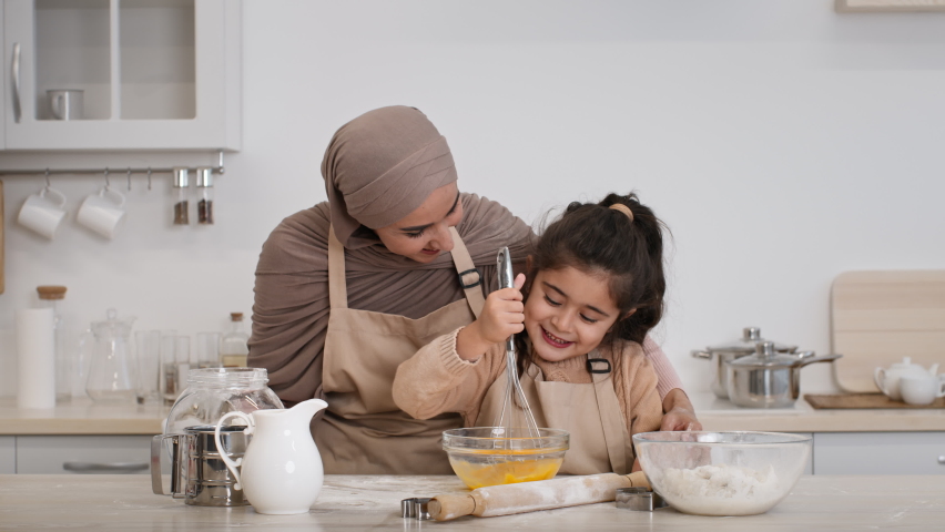 Cheerful Muslim Mother In Hijab And Her Daughter Baking Together Making Dough Mixing Eggs In Bowl In Modern Kitchen Indoors. Middle-Eastern Family Of Two Cooking Cookies On Weekend. Zoom In Royalty-Free Stock Footage #1073810222