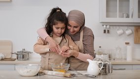 Joyful Muslim Mom And Little Daughter Making Dough Adding Eggs Baking Cookies Together Sitting In Modern Kitchen At Home. Middle-Eastern Mother In Hijab And Her Kid Cooking On Weekend. Zoom In