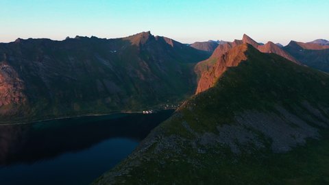Aerial view overlooking mountain peaks, revealing a town, during nightless night, in Senja, Norway - tracking, drone shot