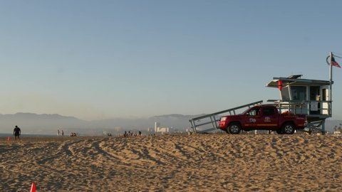 LOS ANGELES CA USA - 16 NOV 2019: California summertime Venice beach aesthetic. Iconic retro wooden lifeguard watchtower, baywatch red car. Life buoy and american state flag near Santa Monica.