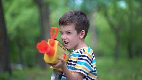 Child boy shoots from toy weapons gun outdoors.