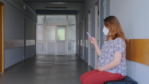 Pregnant woman with phone in clinic lobby with medical mask n95 on face