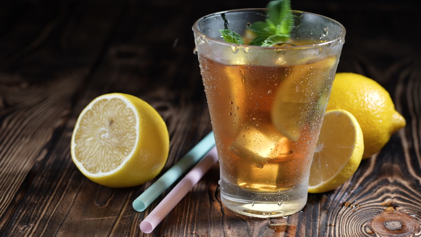 Glass of iced tea with ice cubes and sliced lemon, fresh mint on rustic wooden background. Healthy refreshing lemonade for detoxification, sweet tasty soft drink cold aromatic beverage for summer time Royalty-Free Stock Footage #1073824115