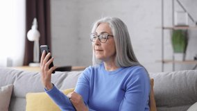 Smiling beautiful elderly gray-haired woman using smartphone for video call. Communication in mobile app at home. Active senior people using modern technology gadget.