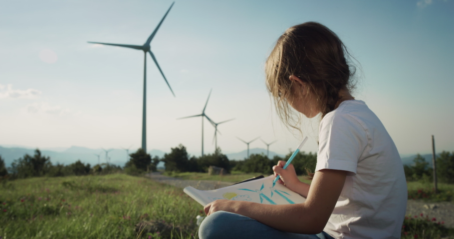 Cinematic shot of happy little girl is drawing wind turbines and enjoying view on windmill field with sun shining. Concept of renewable energy, love for nature, family, electricity, green, future. Royalty-Free Stock Footage #1073825696