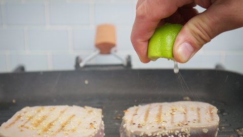 Squeezing a lime juice over a steak of yellowfin tuna on a grilling pan in 4K. Concept seasoning and frying and cooking tuna steak in slow motion.