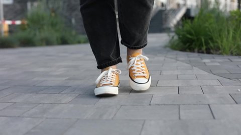 Close up Feet of woman while walking commuting to work. Female in yellow sneakers being walking down the street. Confident girl Feet Walking In City. Girl Legs In in shoes Walking on sidewalk. 