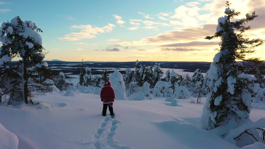 Aerial view over Santa lost between snowy trees, towards a lake, sunset in Lapland - rising, drone shot Royalty-Free Stock Footage #1073833391