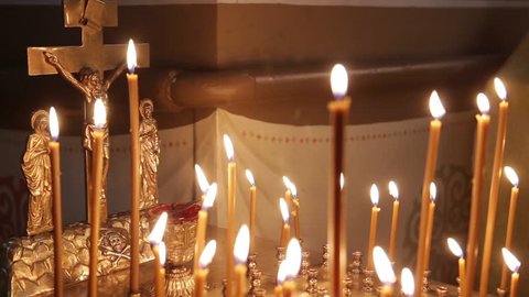 The Orthodox Church. Woman's hand puts the burning candle in front of the symbol of the crucifixion. There is a sound intershum.