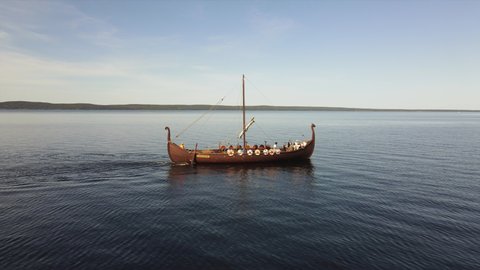 Viking ship with tourists floats on the lake against the blue sky