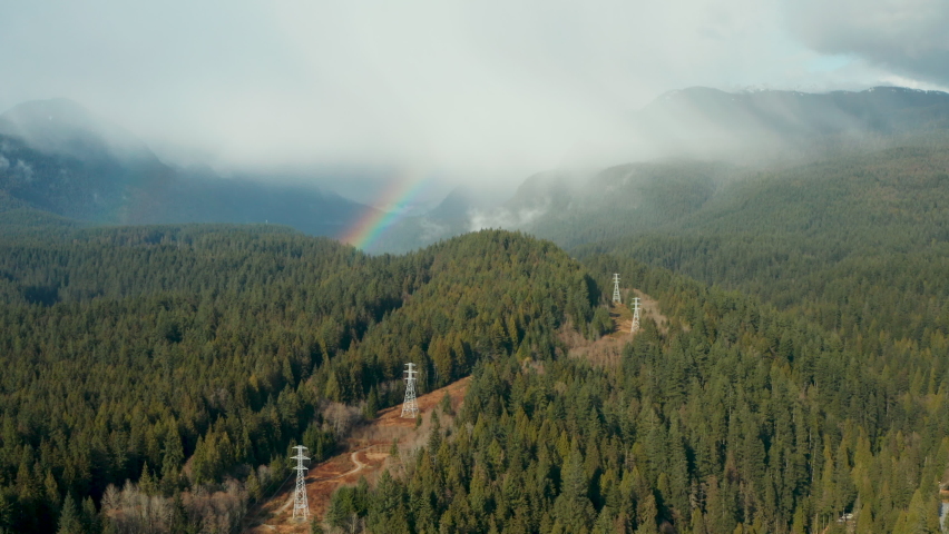 Aerial view of a rainbow piercing the clouds in the scenic British Columbia mountain wilderness.