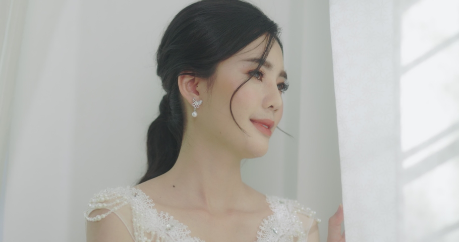 Slow Motion Beautiful Asian Bride Looking Out The Window. The Light From The Window Illuminates A Bride On Her Wedding Day.