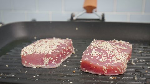Seasoning with salt pepper and sesame seed yellowfin tuna steak on grilling pan. Concept of grilling a tuna steak and sprinkling spices on top in 4K.