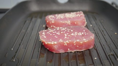 Placing a raw steak of yellowfin tuna into a grilling pan in 4K. Concept frying and cooking tuna steak in slow motion.