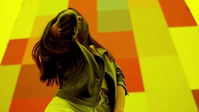 Beautiful , stylish , young girl with black hair and beautiful body in Leather Jacket and sport jeans  dancing , moving , smiling and looking at camera with happy emotions . Slow motion colorful wall