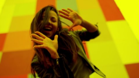 Beautiful , stylish , young girl with black hair and beautiful body in Leather Jacket and sport jeans  dancing , moving , smiling and looking at camera with happy emotions . Slow motion colorful wall