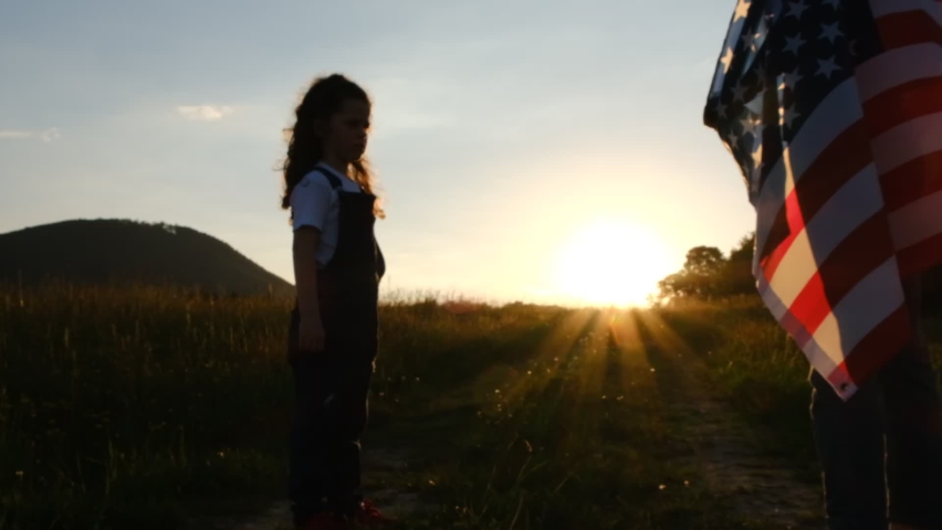 Selective focus of mother with daughter run meadow in wind with united states flag on background mountains during epic sunset. Concept of Memorial Day or 4th of July, Independence Day, Veterans Day Royalty-Free Stock Footage #1073848811